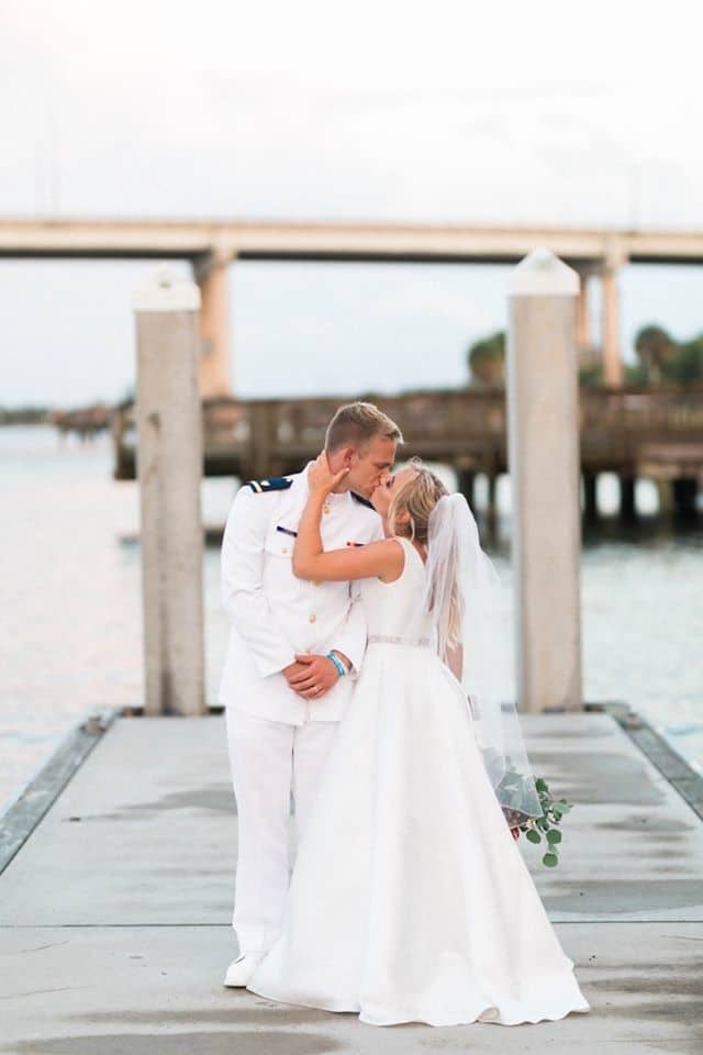 bride and groom kissing on dock outside wedding venue overlooking the water